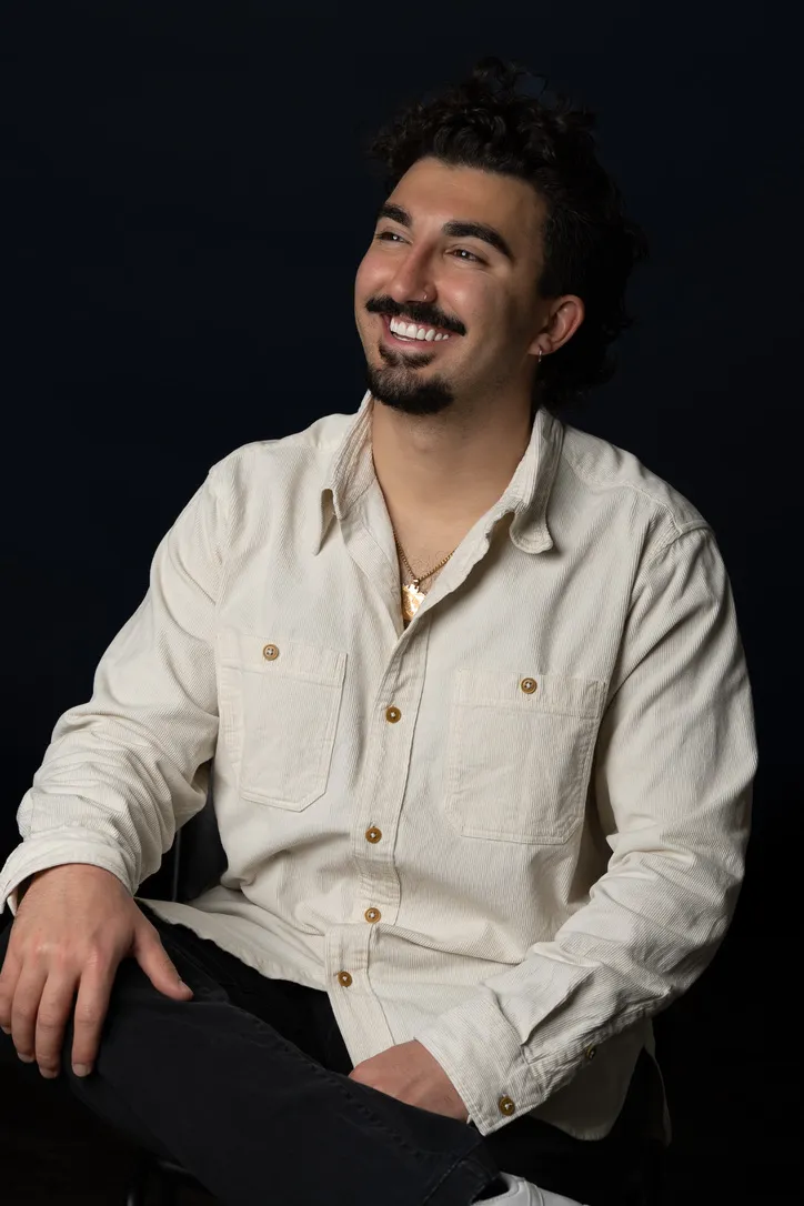 Sean Kraemer, seated in a cream corduroy shirt against a dark background, laughing off-camera